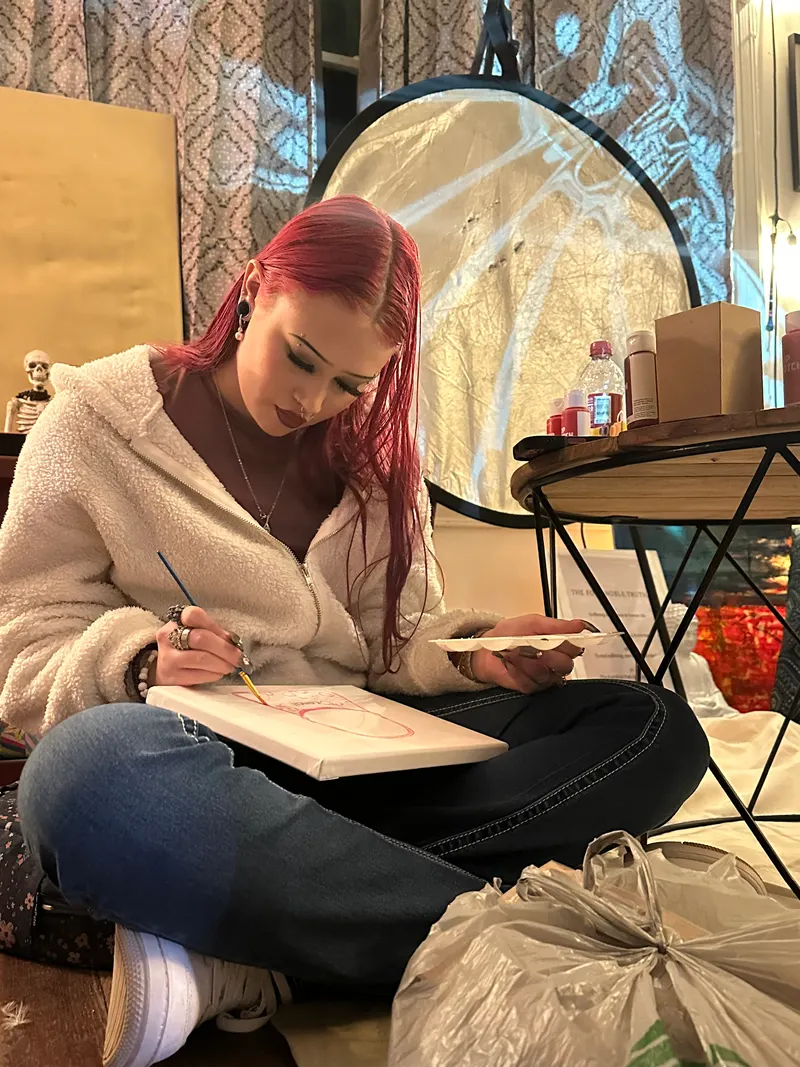 A woman sits cross-legged sketching on paper
