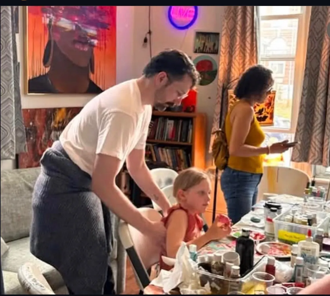 A volunteer helps a child get settled at the art table under the neon LIVE sign